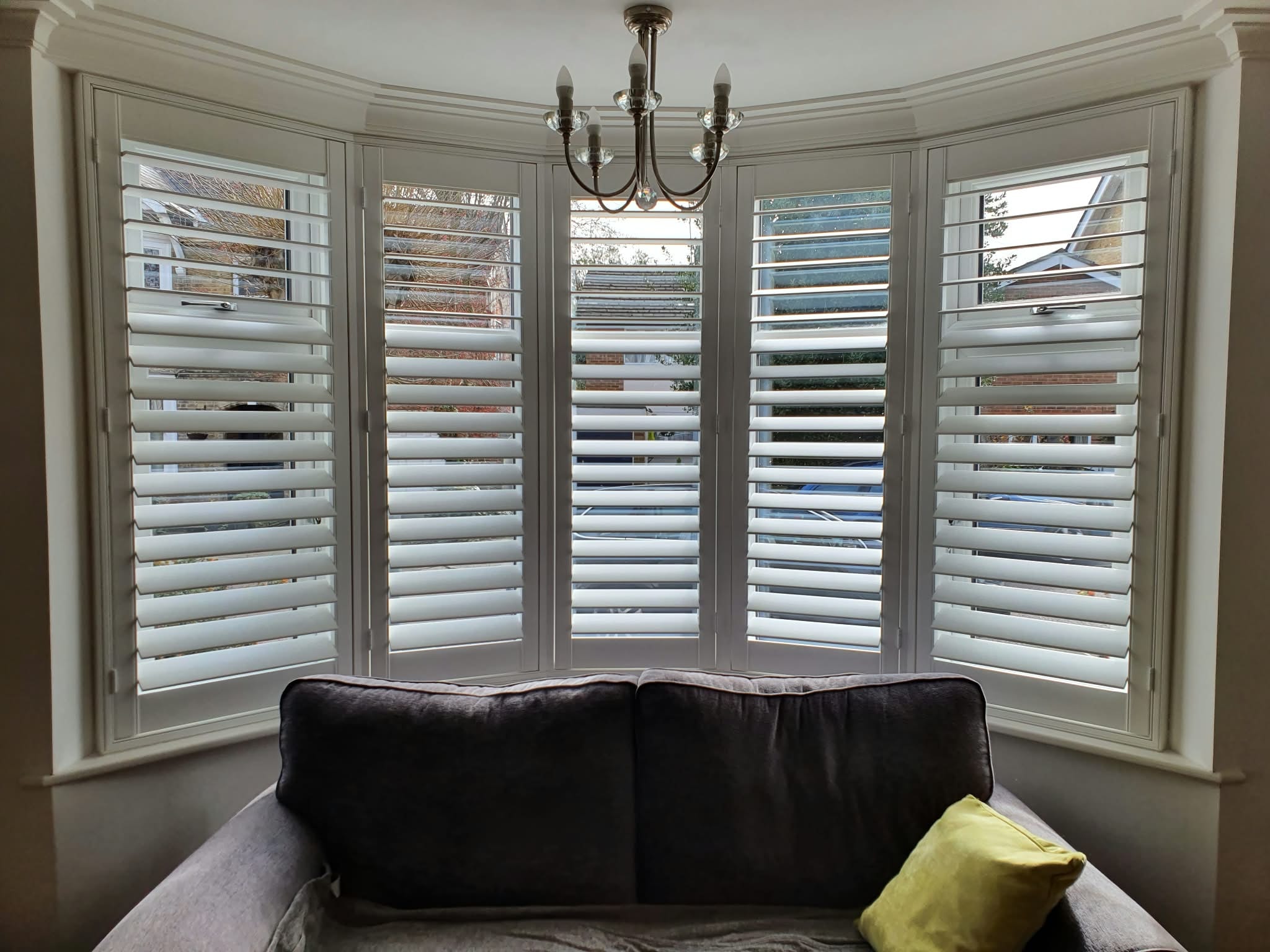 White shutters in a bay window living room — Sustainable Shutters & Blinds