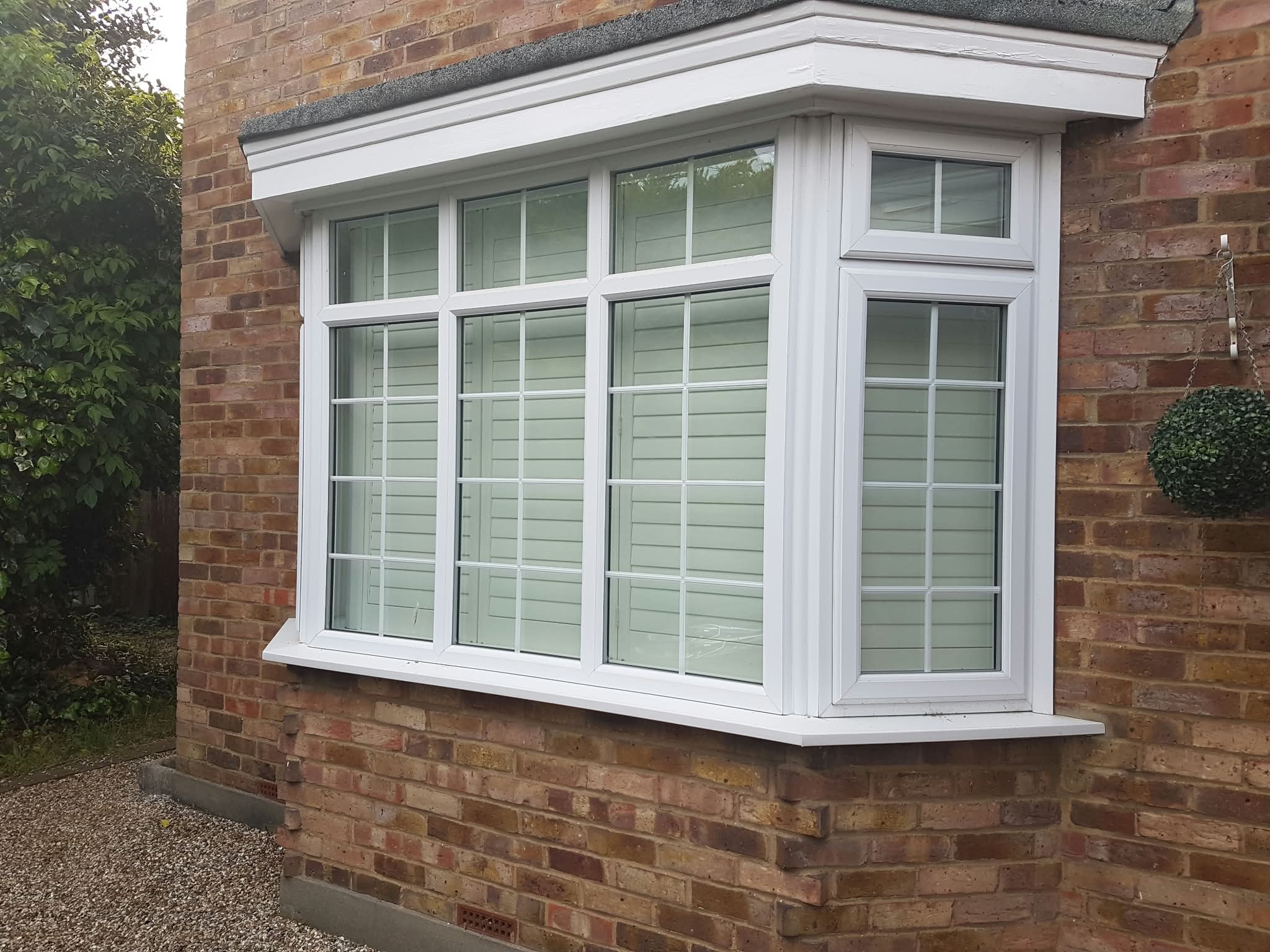 White bay window shutters on a brick house exterior — Sustainable Shutters & Blinds