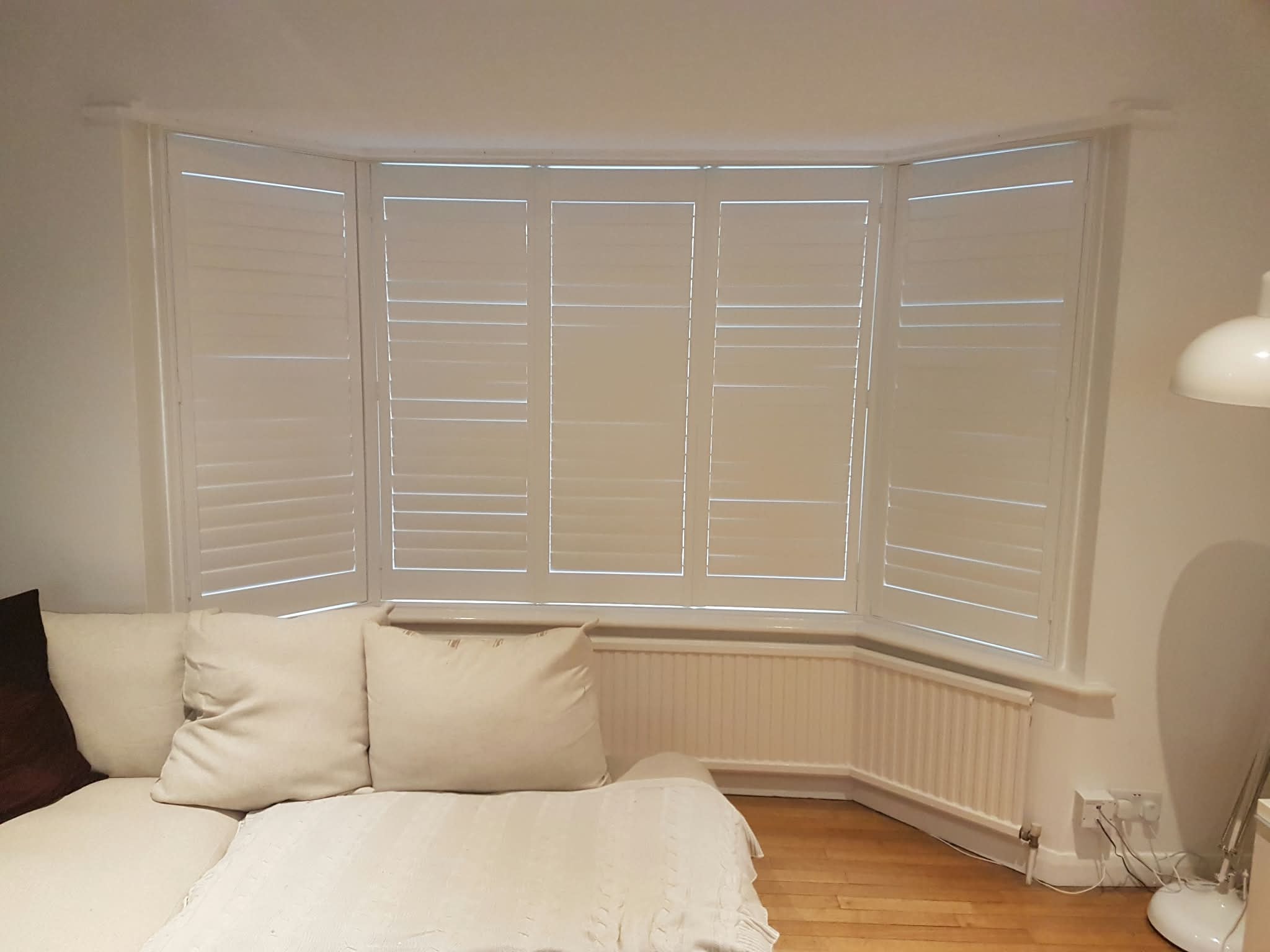 White shutters in a bay window bedroom — Sustainable Shutters & Blinds