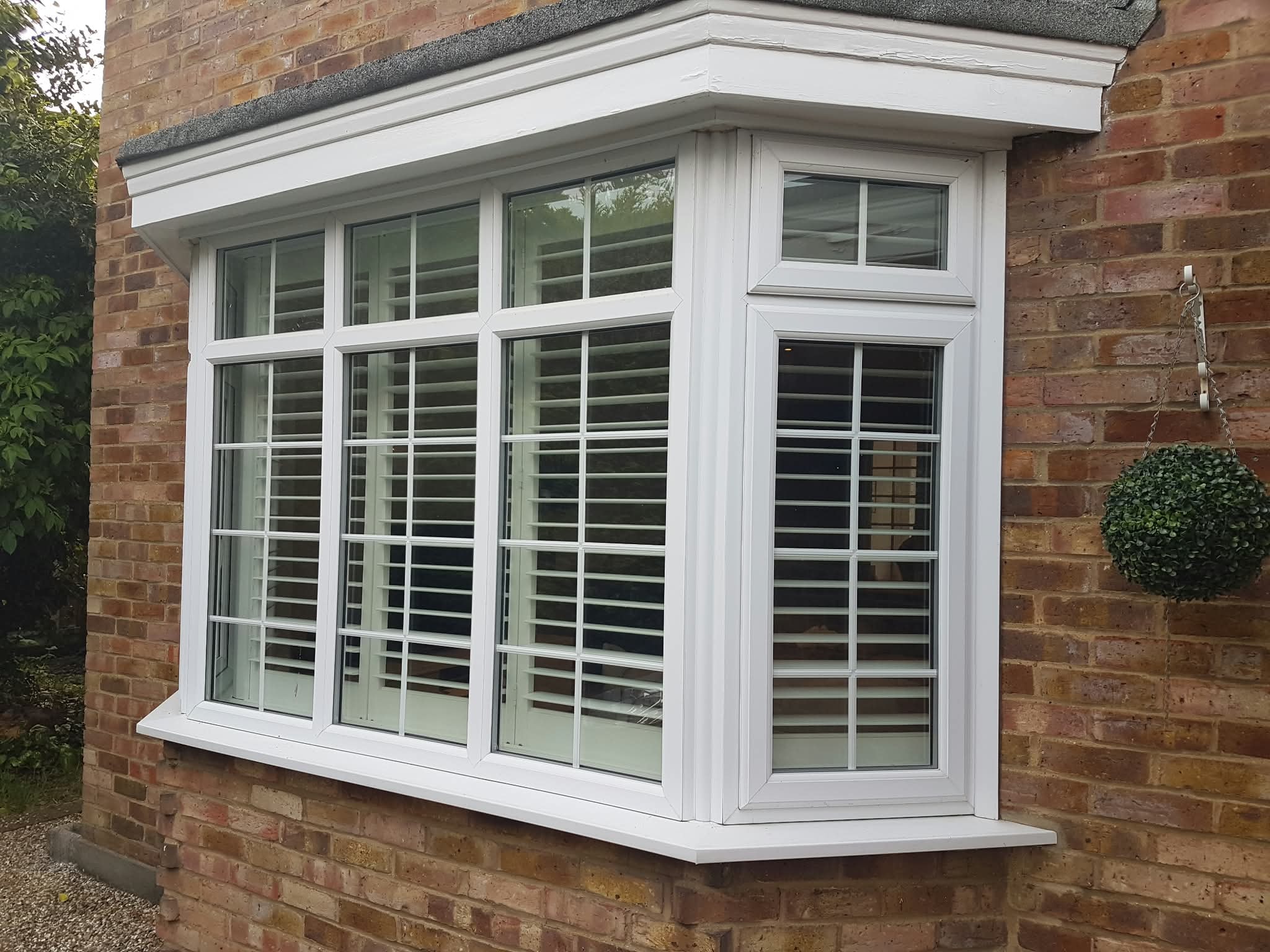 White bay window shutters on a brick house exterior — Sustainable Shutters & Blinds