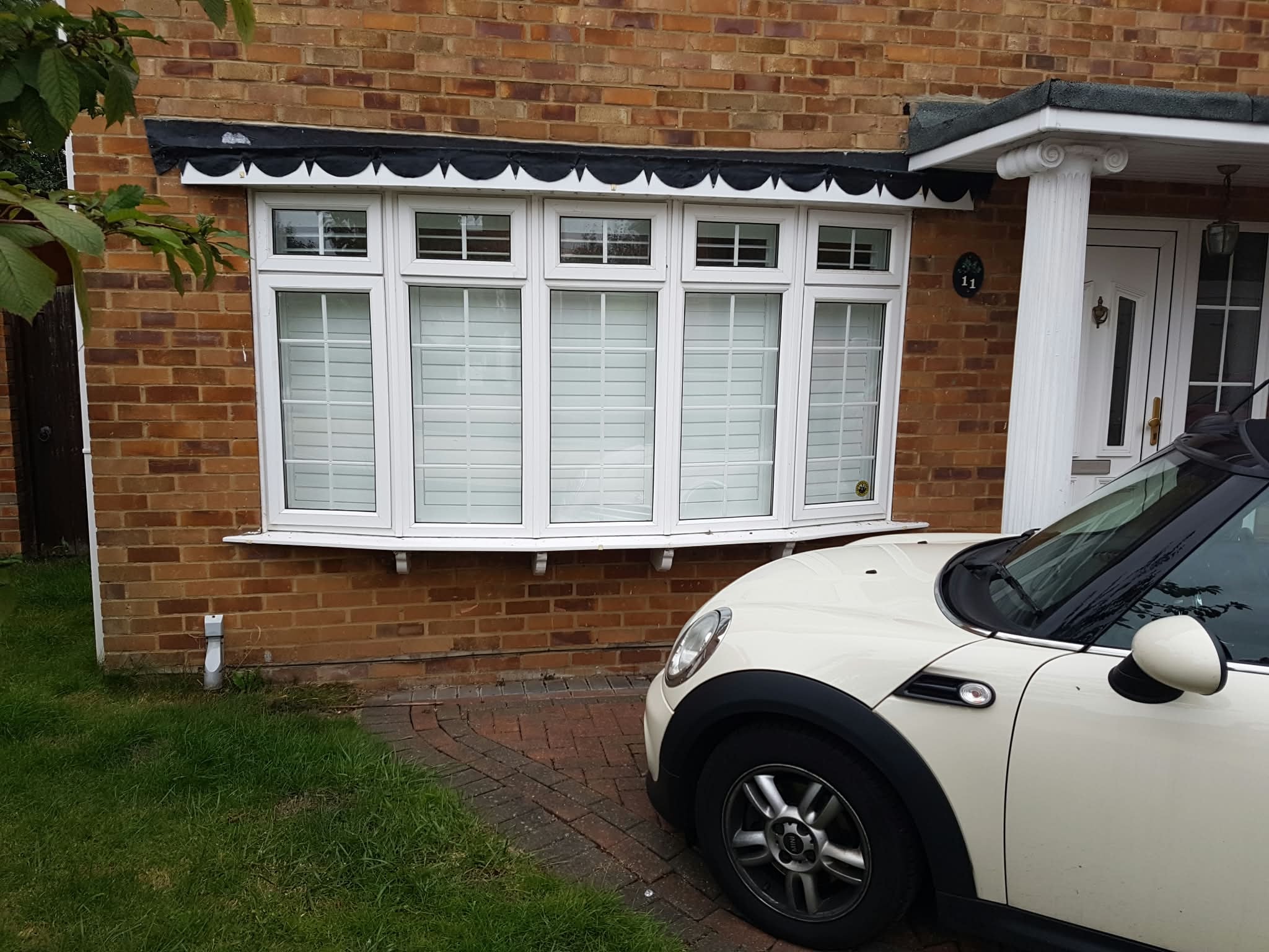 White bay window shutters on a brick house exterior — Sustainable Shutters & Blinds
