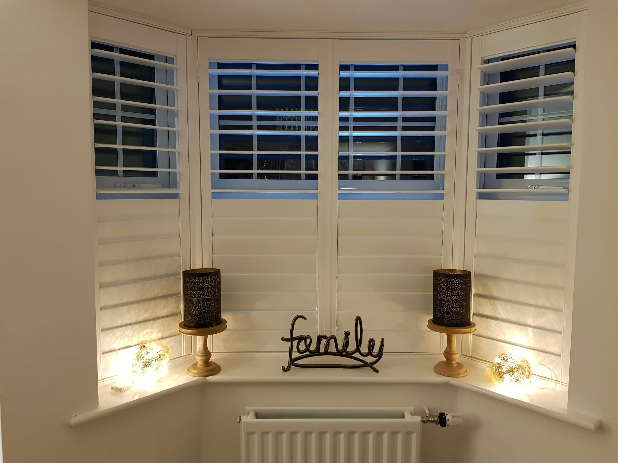 Shutters on a bay window with candles on the sill — Sustainable Shutters & Blinds