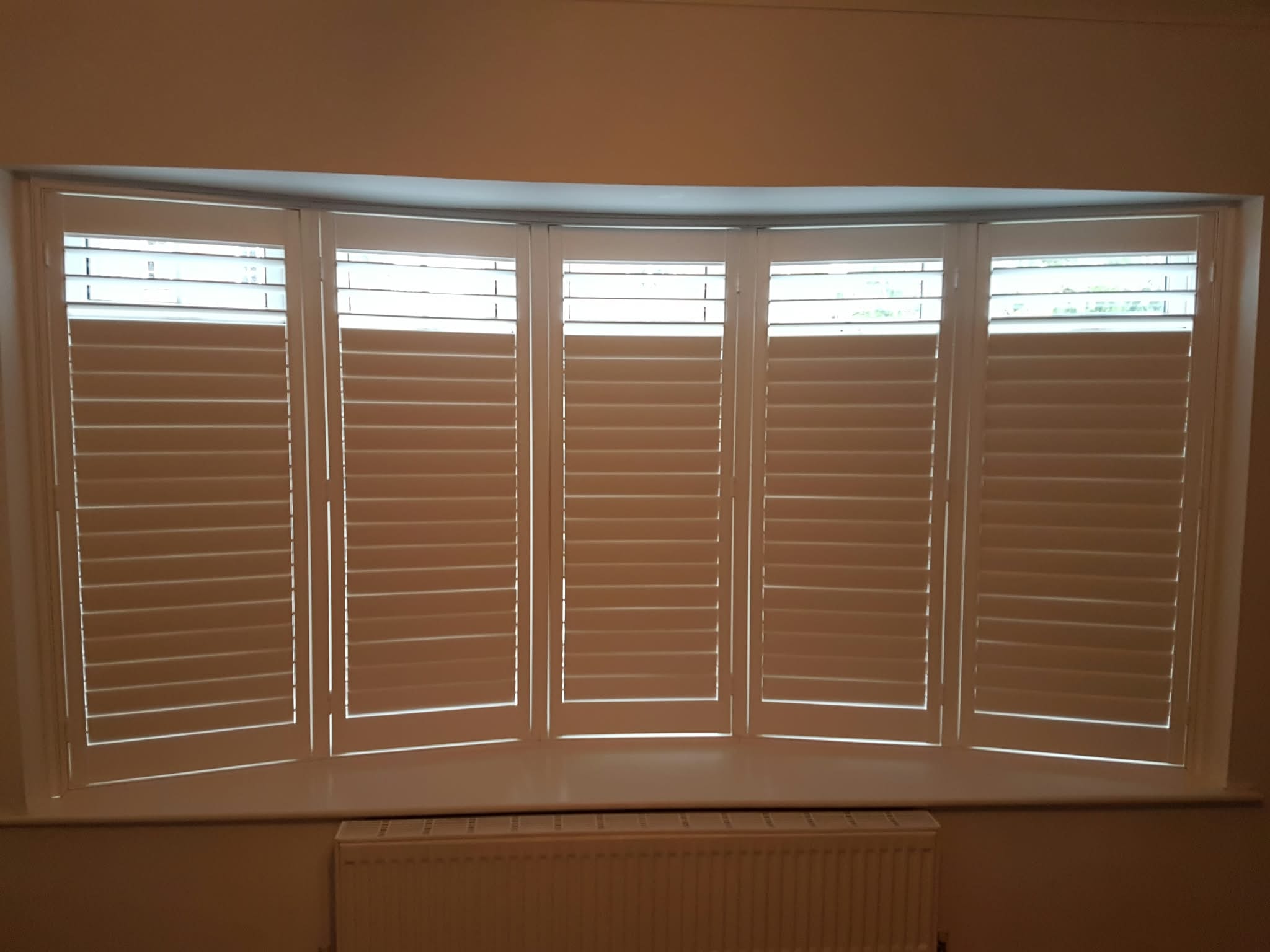 Five-panel shutters on a curved bay window — customer installation by Sustainable Shutters