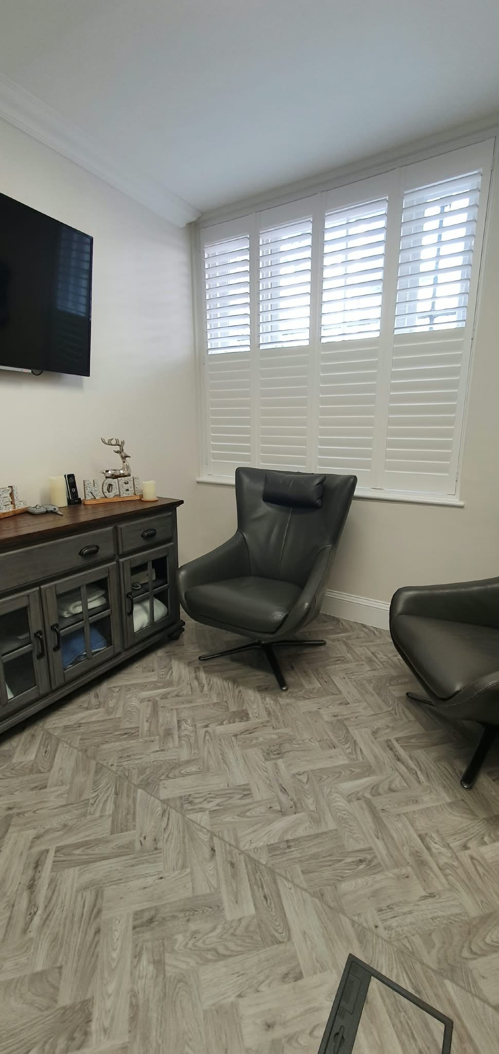 White shutters in a living room with leather chairs and herringbone floor — Sustainable Shutters & Blinds