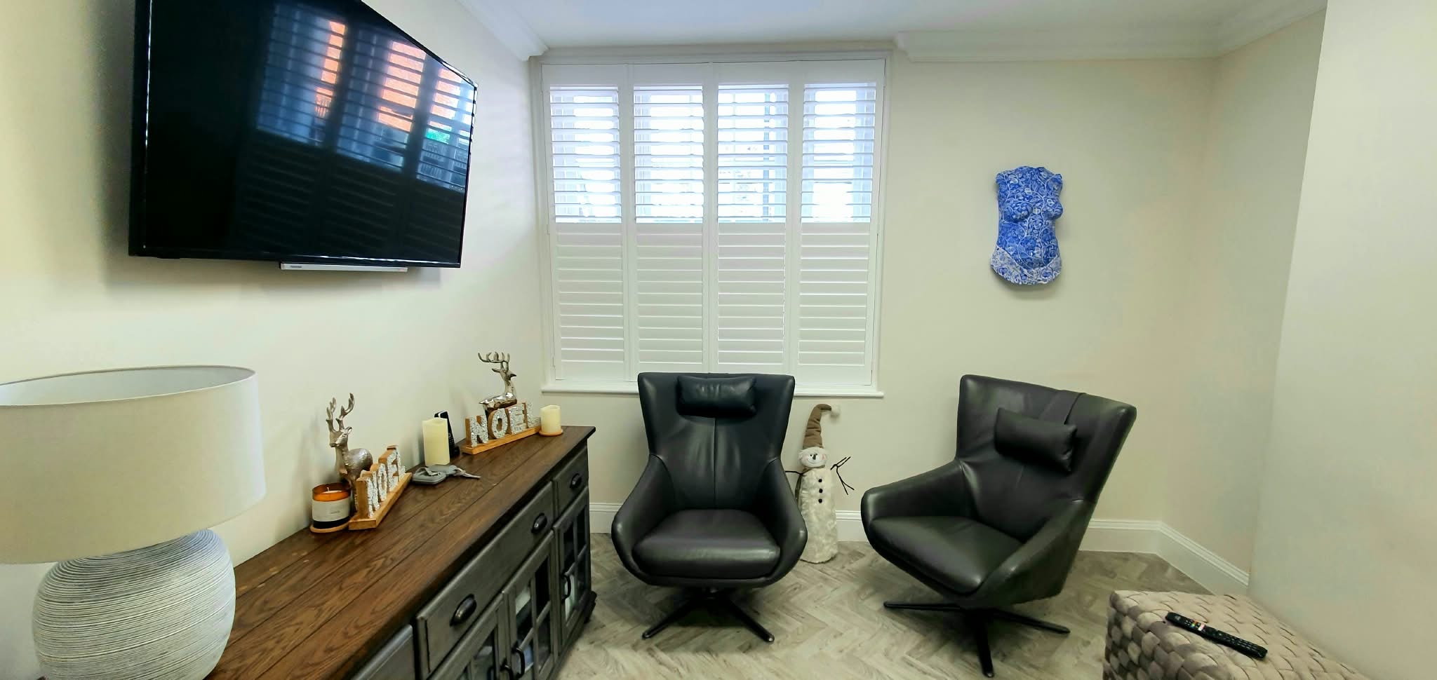 White shutters in a living room with two leather chairs — Sustainable Shutters & Blinds