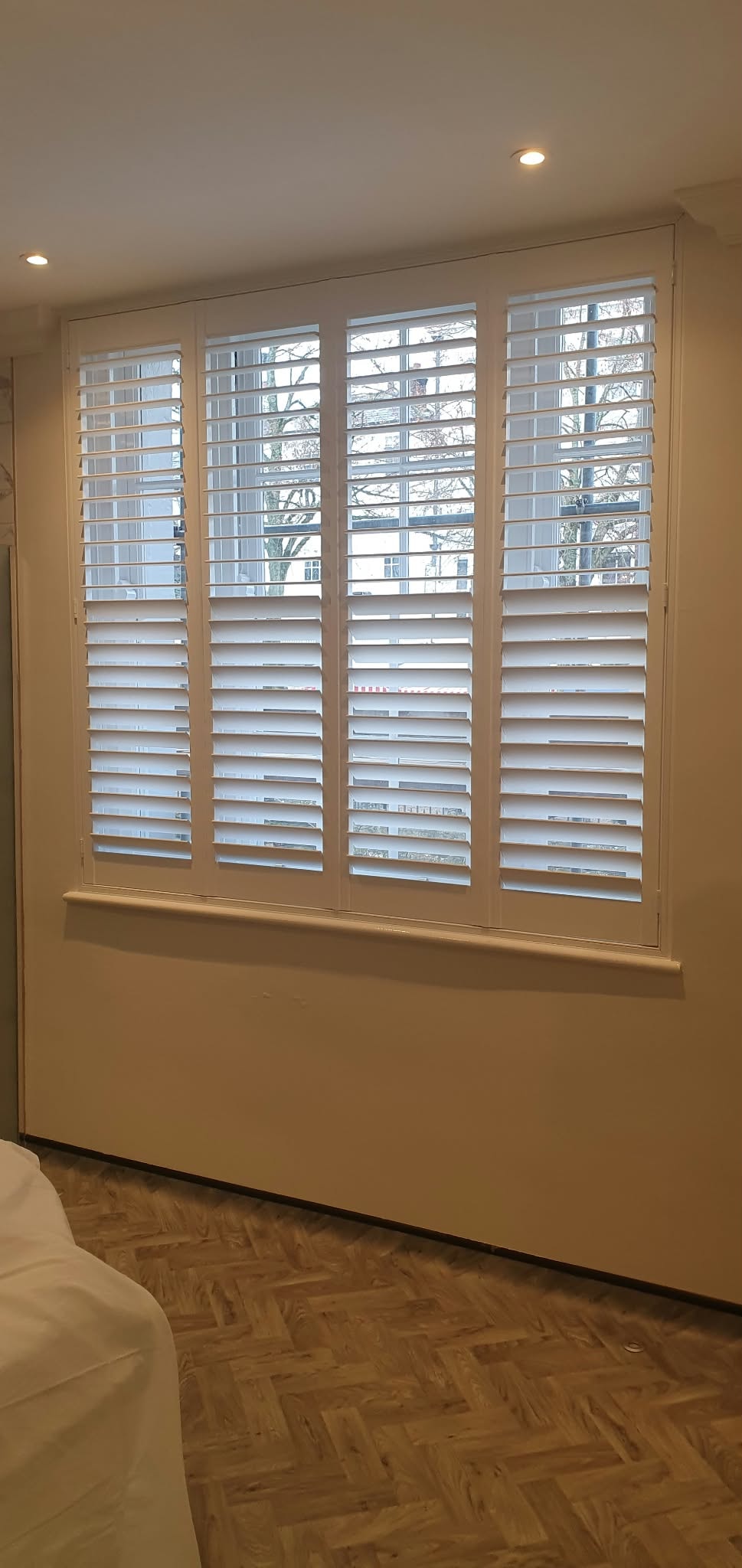 Full-height white shutters in a bedroom with parquet floor — customer installation by Sustainable Shutters