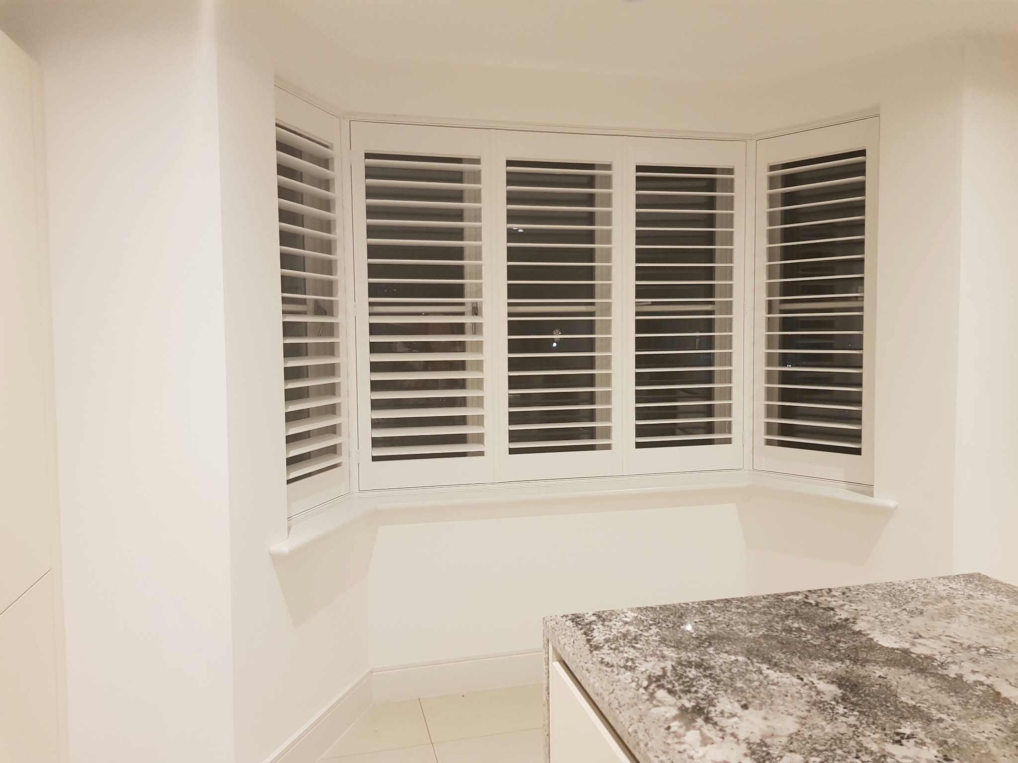 White shutters on a curved bay window in a kitchen — Sustainable Shutters & Blinds