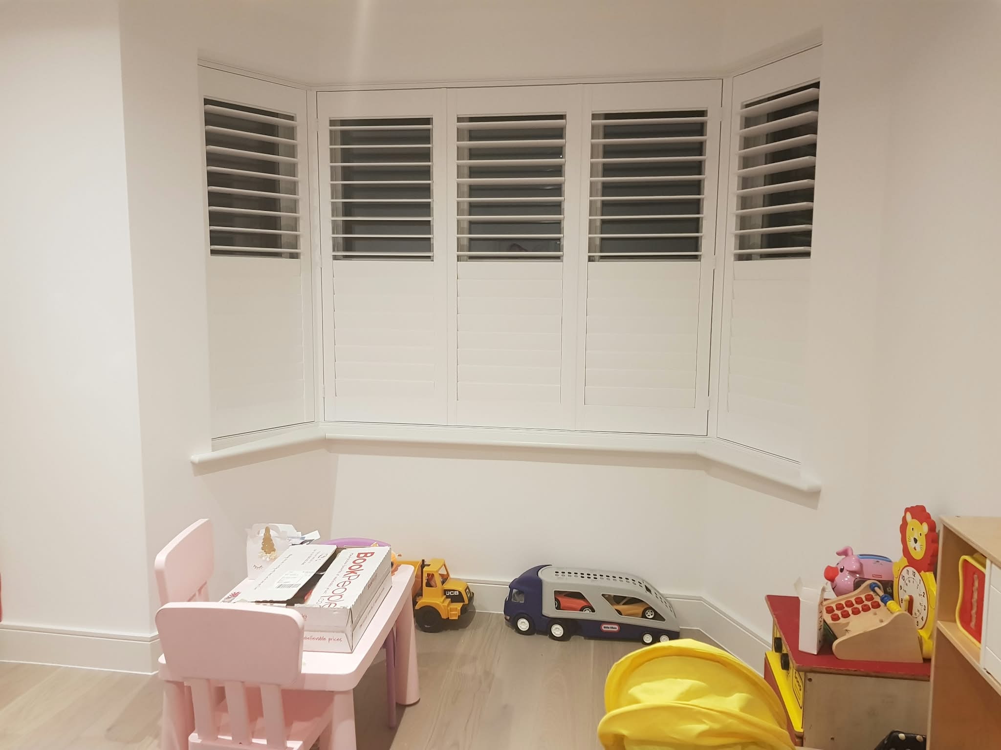 White shutters on a bay window in a children's playroom — Sustainable Shutters & Blinds