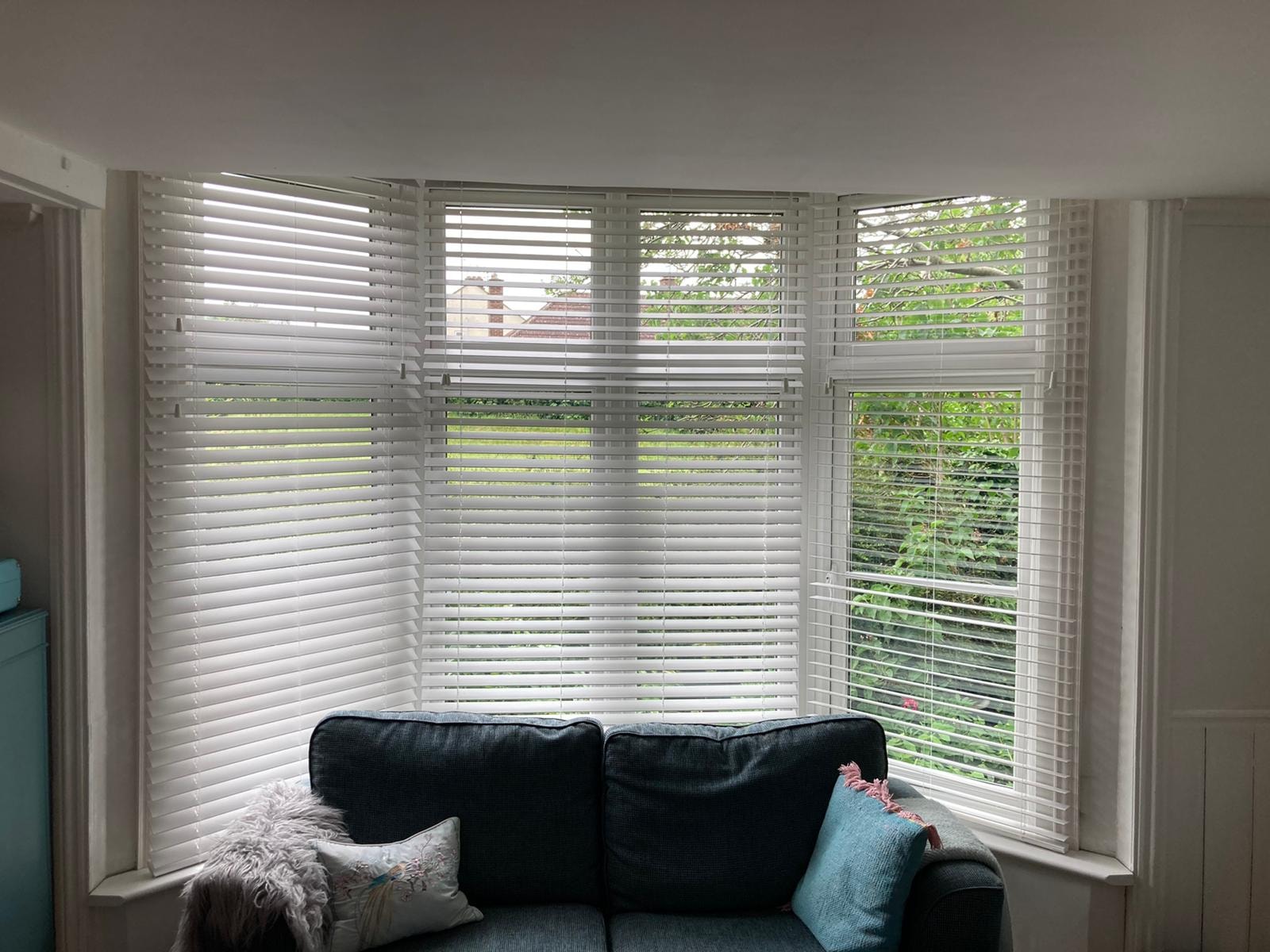 White Venetian blinds on a bay window above a sofa — Sustainable Shutters & Blinds