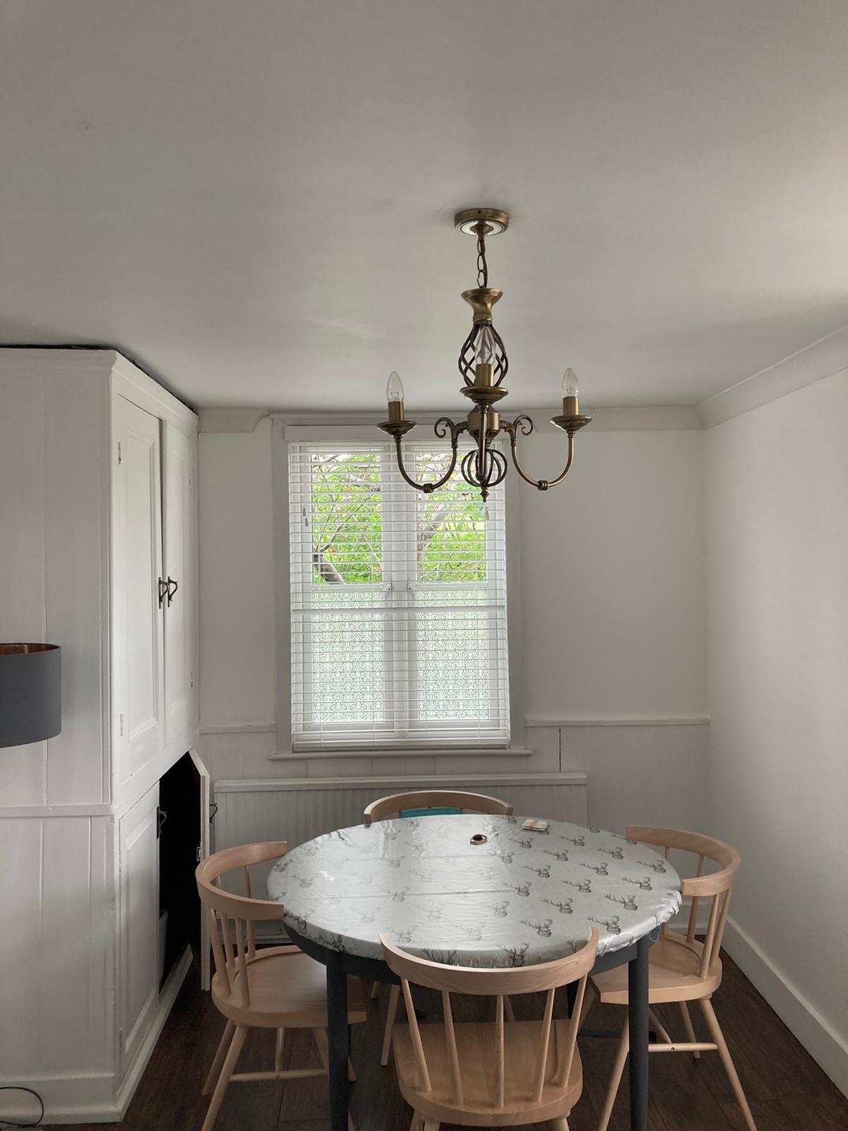 White Venetian blind in a dining room with brass chandelier — customer installation by Sustainable Shutters