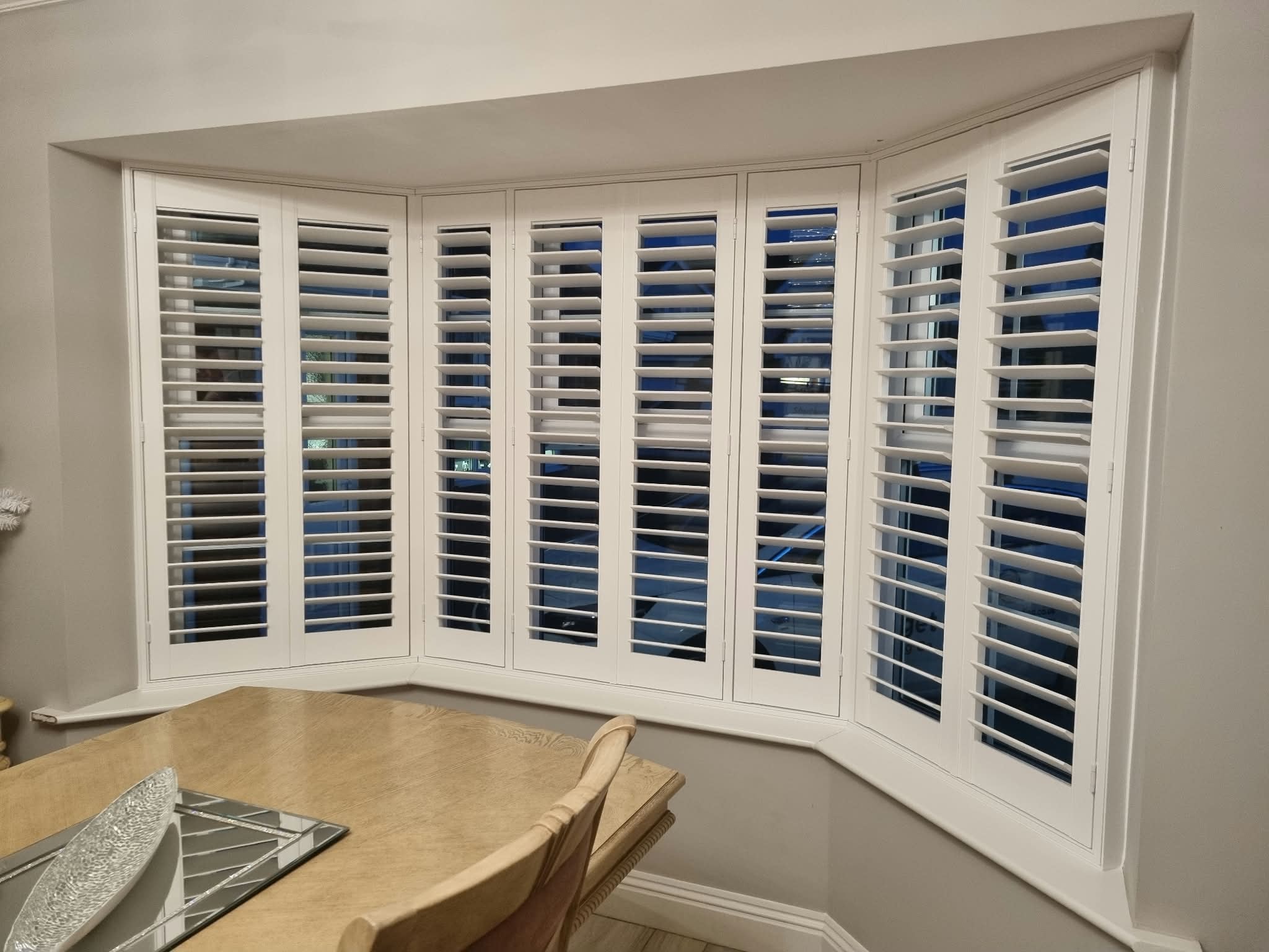 White plantation shutters on a curved bay window — Sustainable Shutters & Blinds
