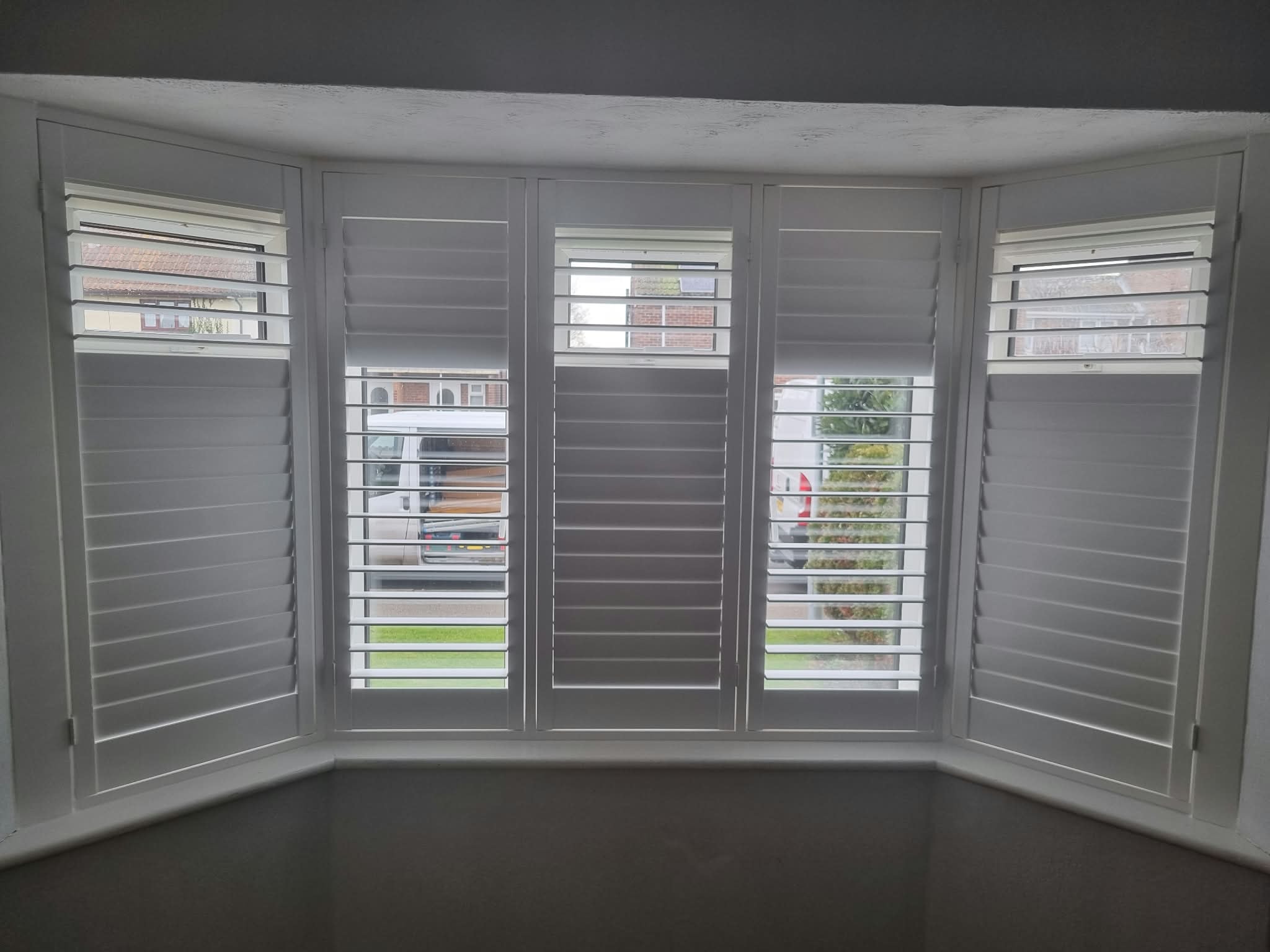 White plantation shutters on a bay window interior — Sustainable Shutters & Blinds